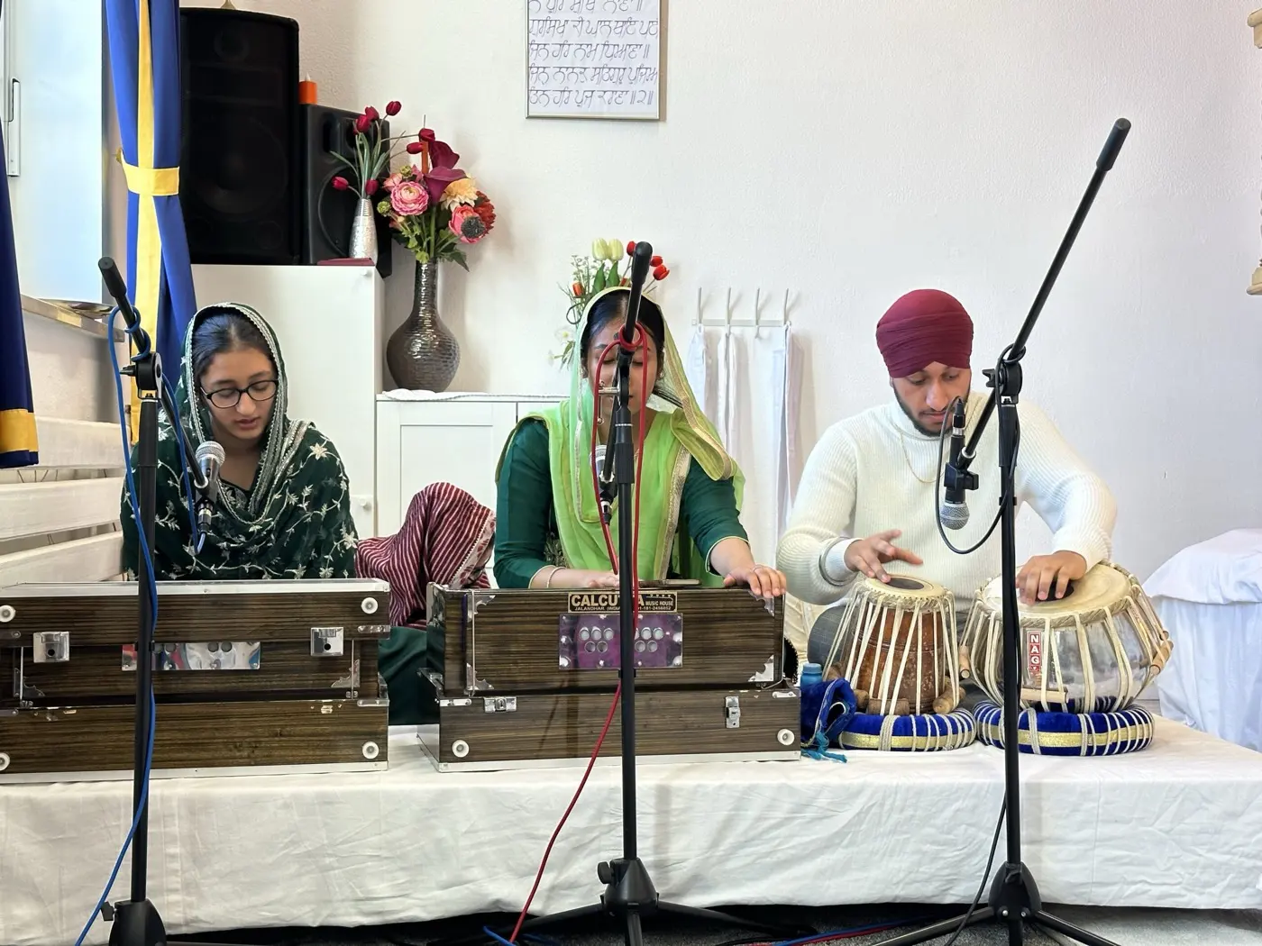 Drei Gemeindemitglieder singen Kirtan, begleitet von Harmonium und Tabla