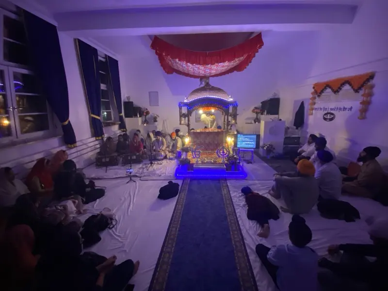 Rainsbai Kirtan (Rain Sabai) im Gurdwara Sahib Kiel: Die Sangat sitzt bei blauem Licht vor dem Palki Sahib und hört Kirtan